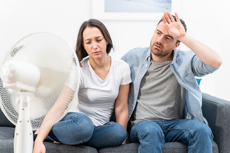 couple trying to stay cool on their couch during a heat wave.